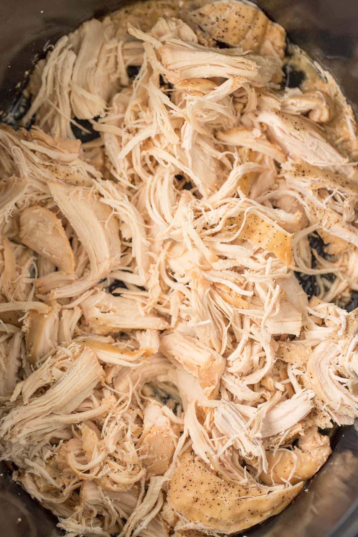 A close up of crockpot shredded chicken in a black crockpot