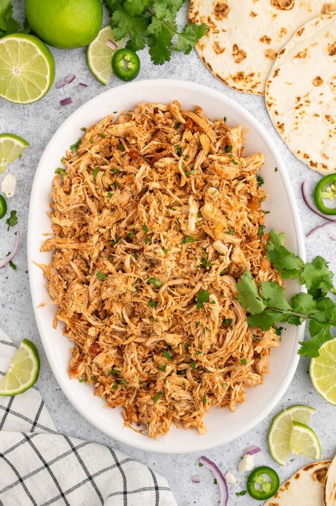 A white platter of shredded chicken for crockpot chicken tacos on a grey background.