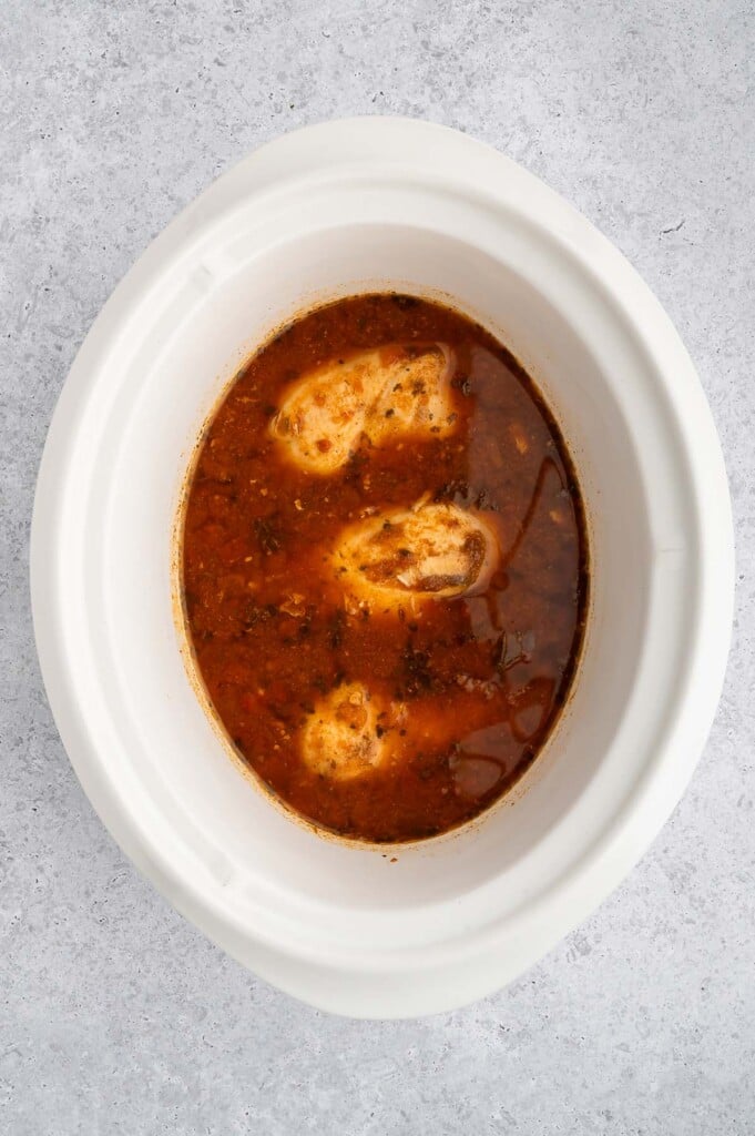 Cooked chicken breasts in a white crockpot base to make crockpot chicken tacos.