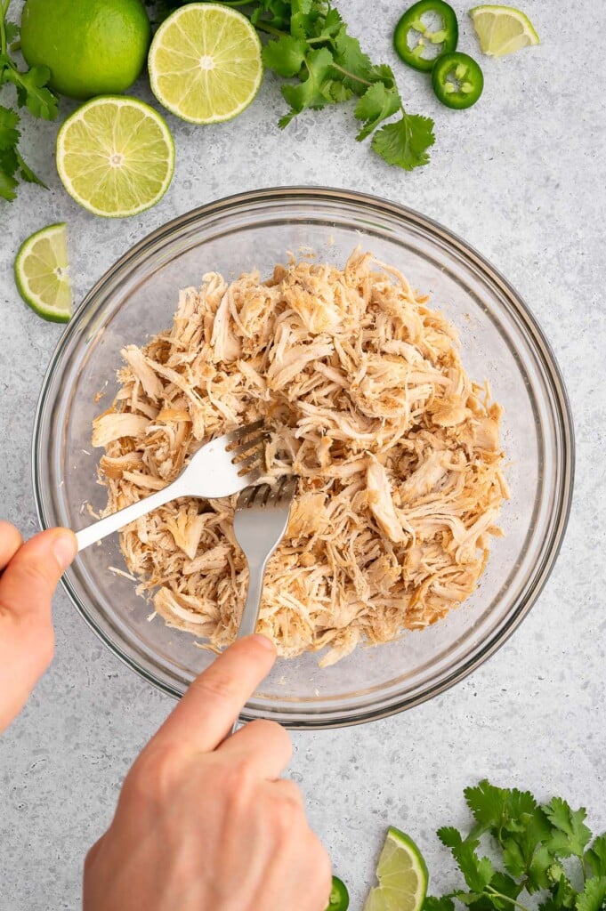 Two forks shredding chicken in a bowl for crockpot chicken tacos.