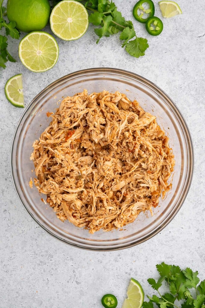 Crockpot shredded chicken for tacos in a bowl on a grey background.