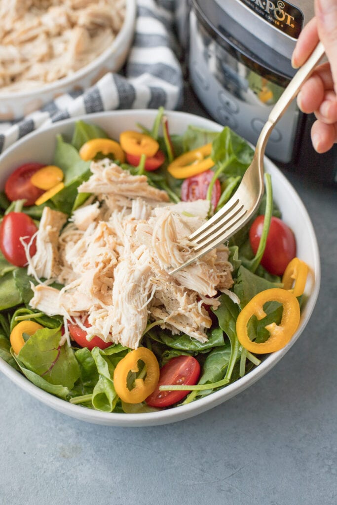 Crockpot shredded chicken on a salad with tomatoes and peppers in a white bowl on a grey background with fork