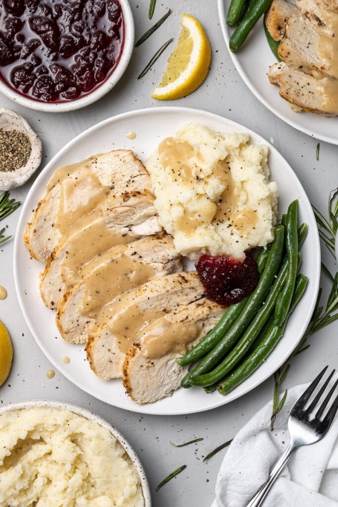 Crockpot turkey breast with gravy on top on a white plate with mashed potatoes and green beans 