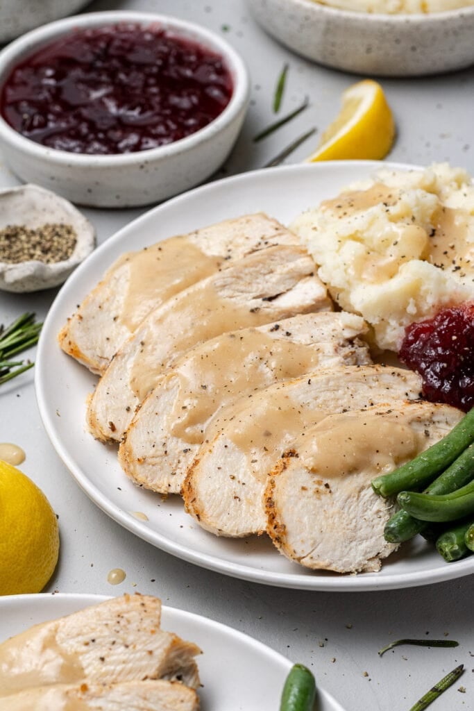 crockpot turkey breast with gravy on top on a white plate with mashed potatoes and green beans