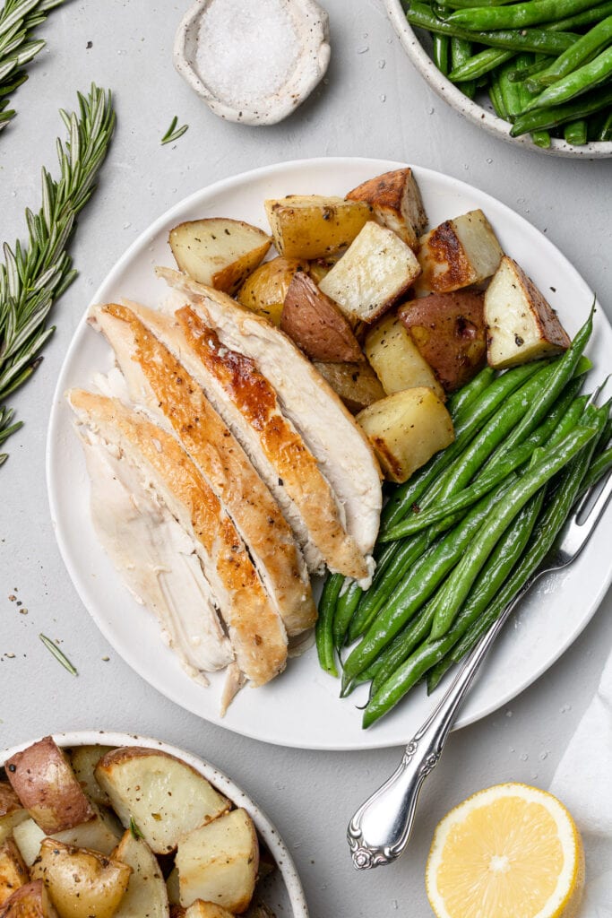 an overhead shot of Crockpot Whole Chicken sliced on a white plate with veggies and potatoes that have been cooked in a slow cooker