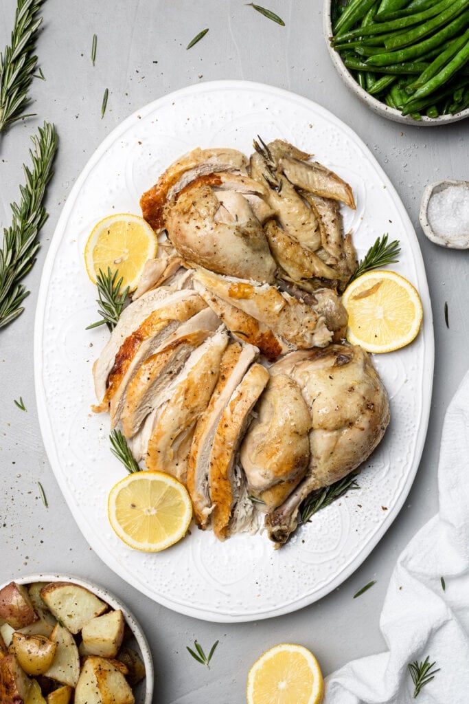 Crockpot Whole Chicken Sliced on a white platter after being cooked in slow cooker on a grey background