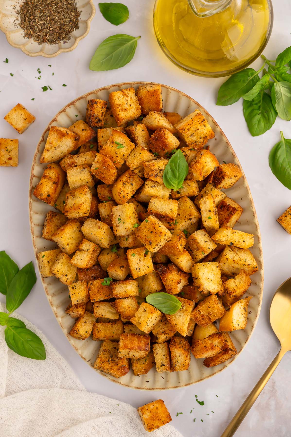 Homemade croutons piled on a platter with fresh basil leaves around it.