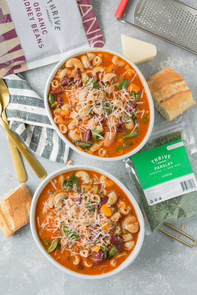 An overhead shot of two bowls of Vegan Minestrone Soup with dried spices, beans and cheese off to the side.