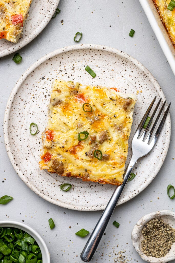 A piece of egg hash brown casserole on a white plate with a fork on the side
