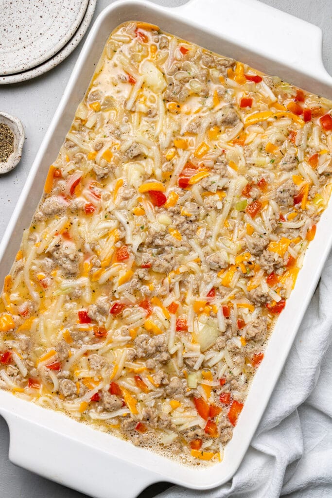 Ingredients for egg hash brown casserole in a white baking dish mixed together prior to baking