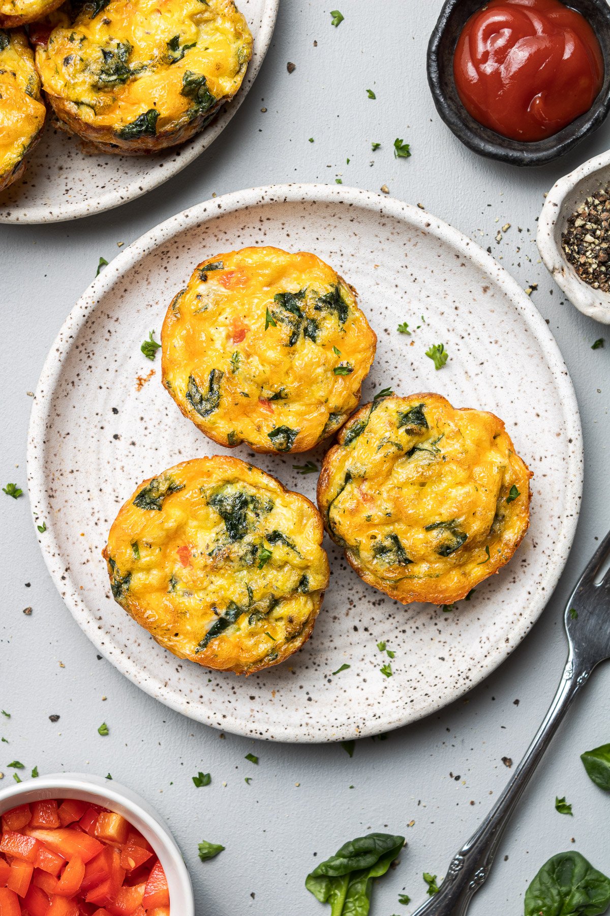 An overhead shot of a plate of three egg muffin cups with more on the side on a grey background