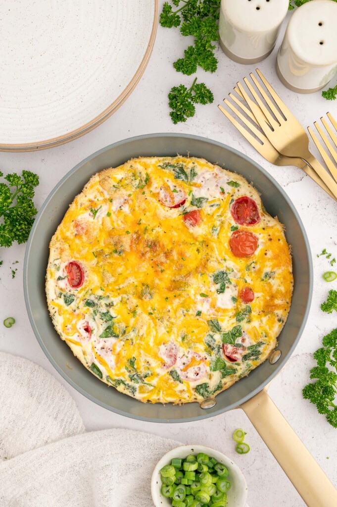 An egg white frittata in a pan with herbs on the side.