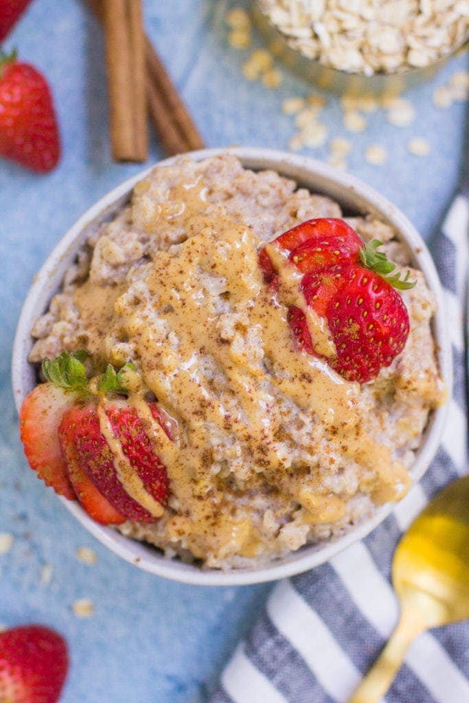 a white bowl filled with egg white oatmeal, topped with strawberries and nut butter