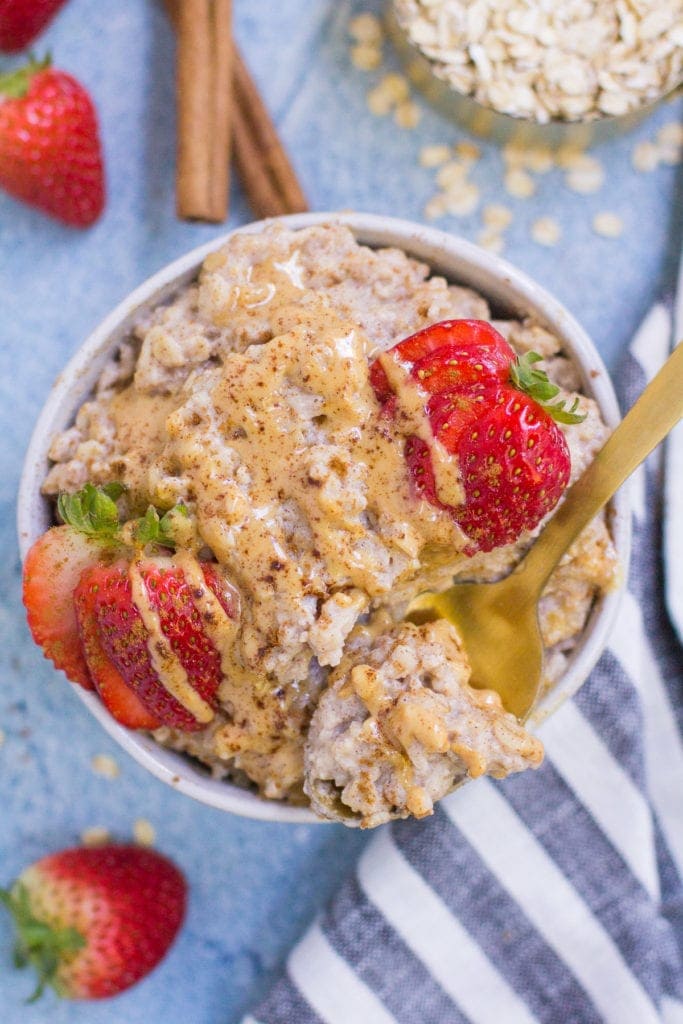A small white bowl filled with egg white oatmeal with a gold spoon off to the side taking a spoon out of it.