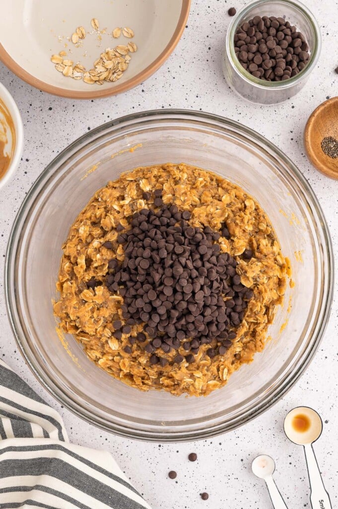 Mini chocolate chips in a pile on top of batter for peanut butter energy balls in a clear bowl before being mixed in