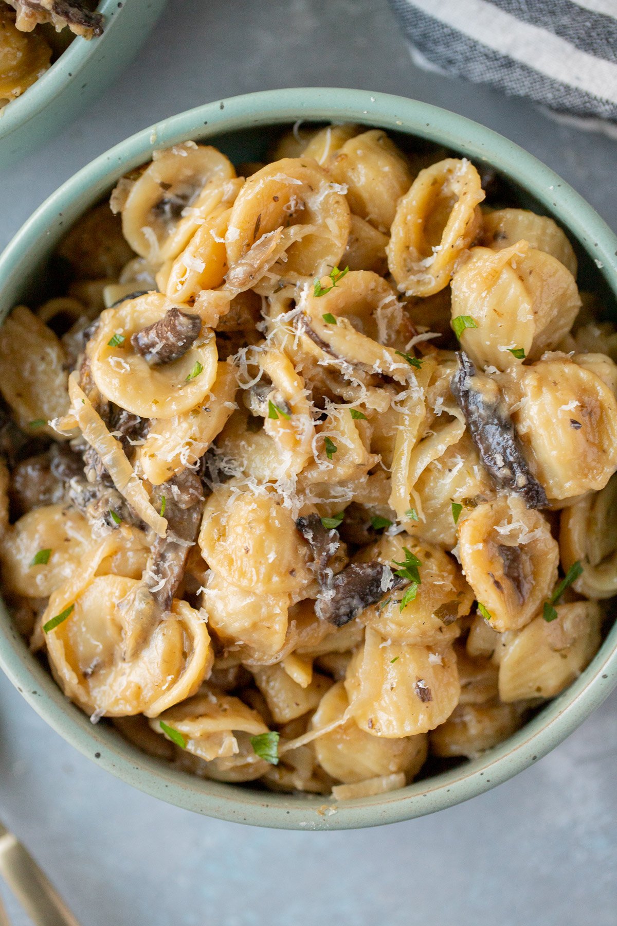 An overhead shot of a blue bowl of french onion pasta on a grey background