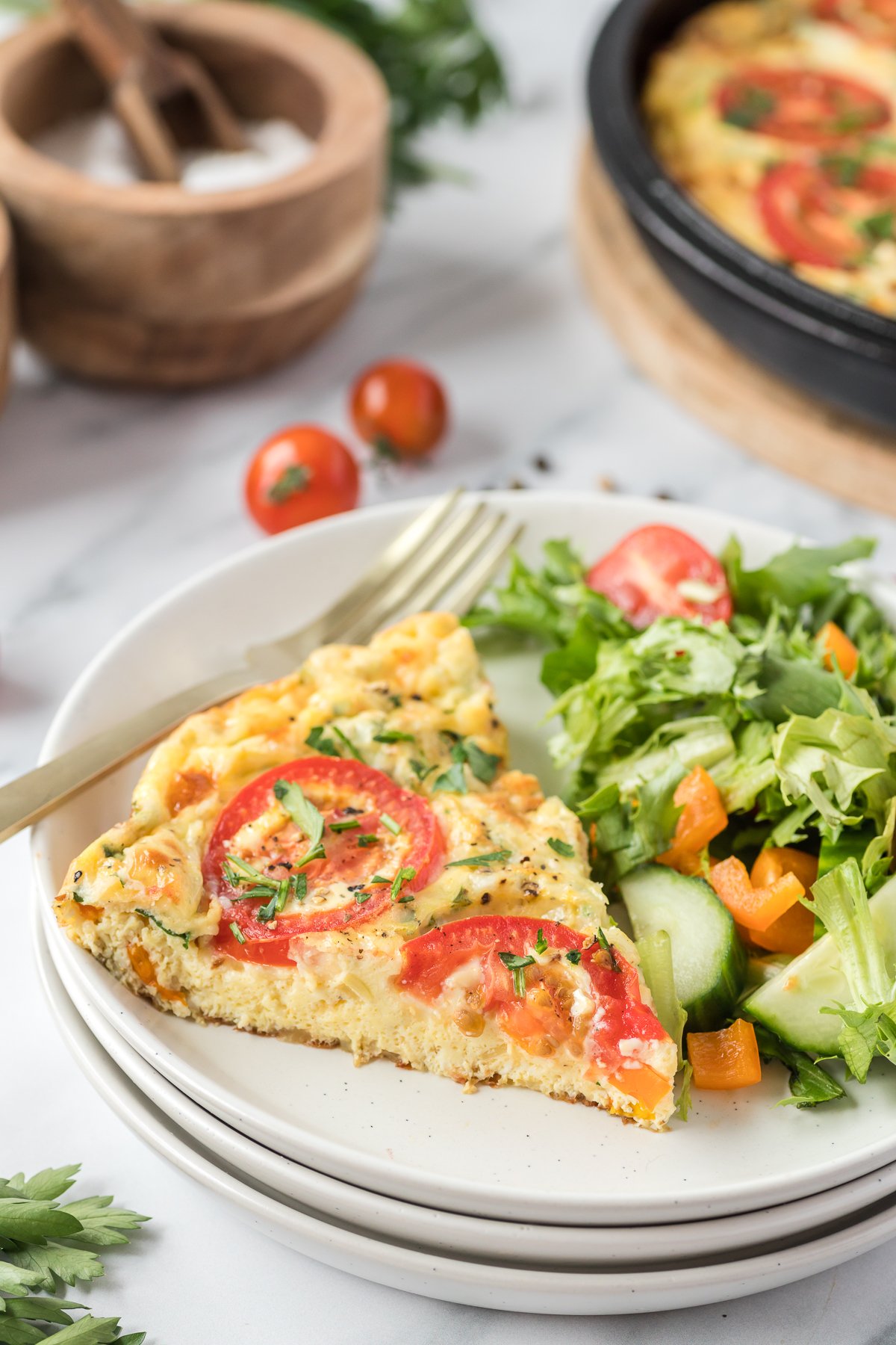 A slice of vegetable frittata on a white plate with a salad on the side