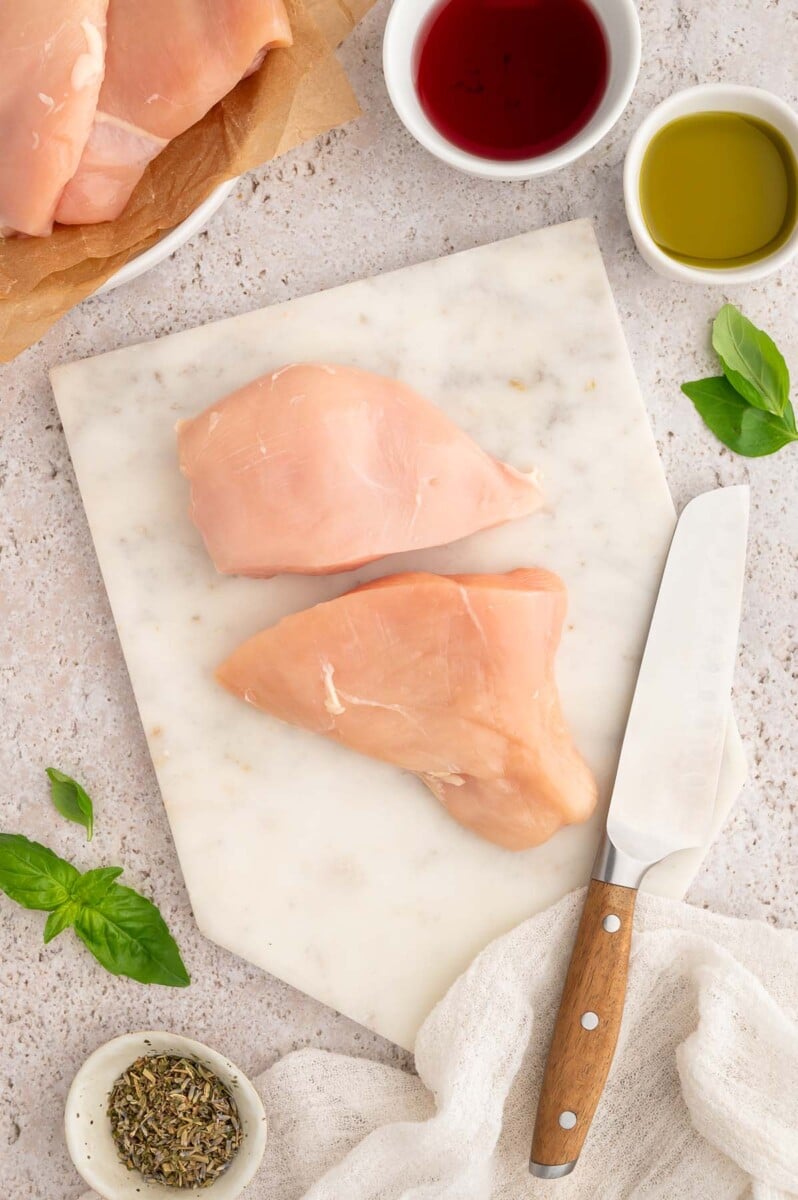 A sliced chicken breast on a cutting board with a knife on the side.