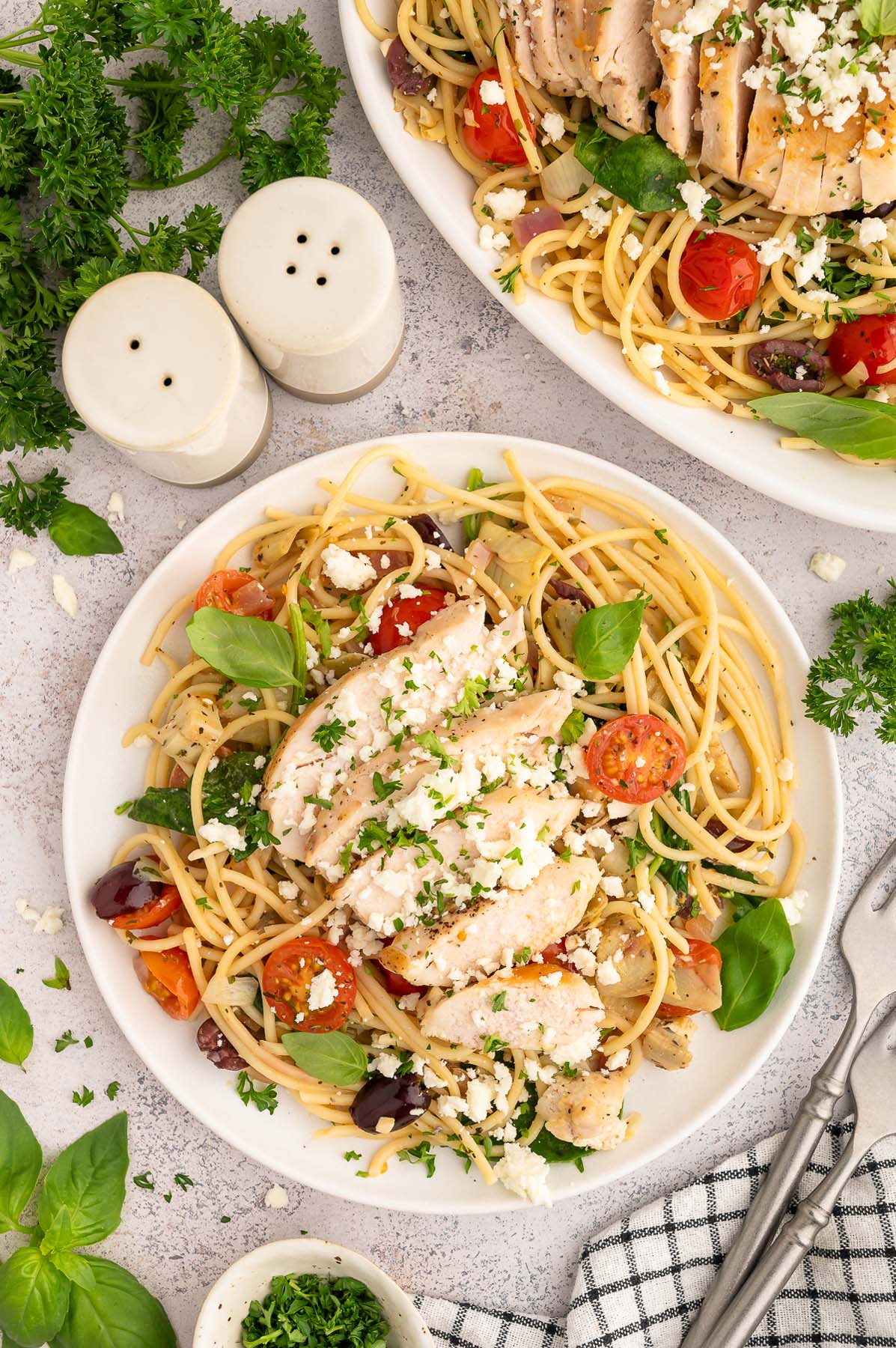 A plate of Greek spaghetti topped with chicken and a plate of spaghetti on the side.