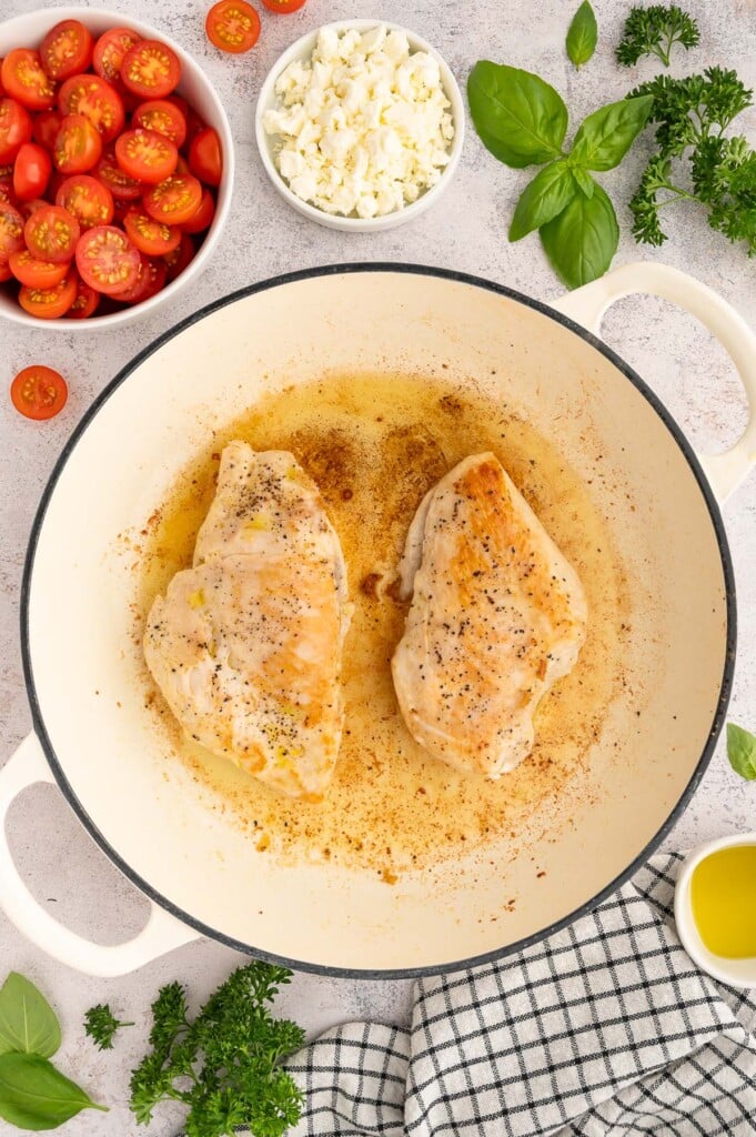 Chicken Breasts cooking in a dutch oven with tomatoes, feta cheese and fresh basil on the side.