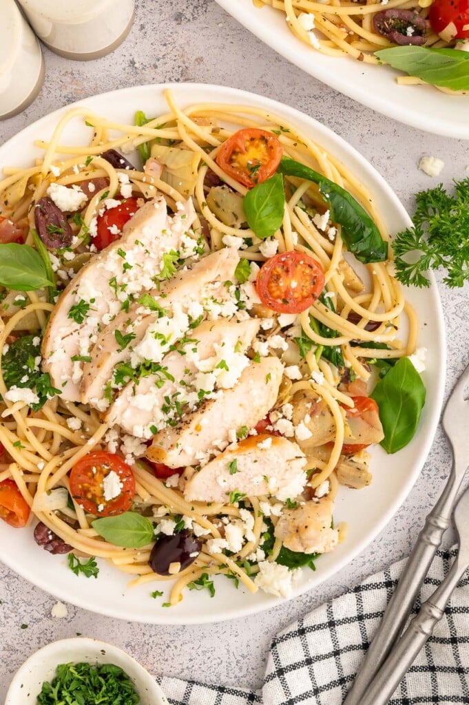 A white plate of Greek spaghetti topped with sliced chicken.
