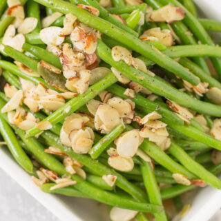 A white serving dish piled high with green beans almondine.