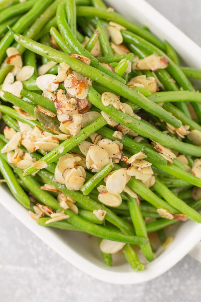 A white serving dish piled high with green beans almondine.
