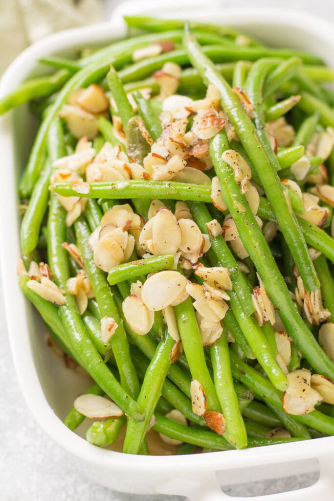 A straight on photo of a white serving dish filled with healthy green beans almondine.