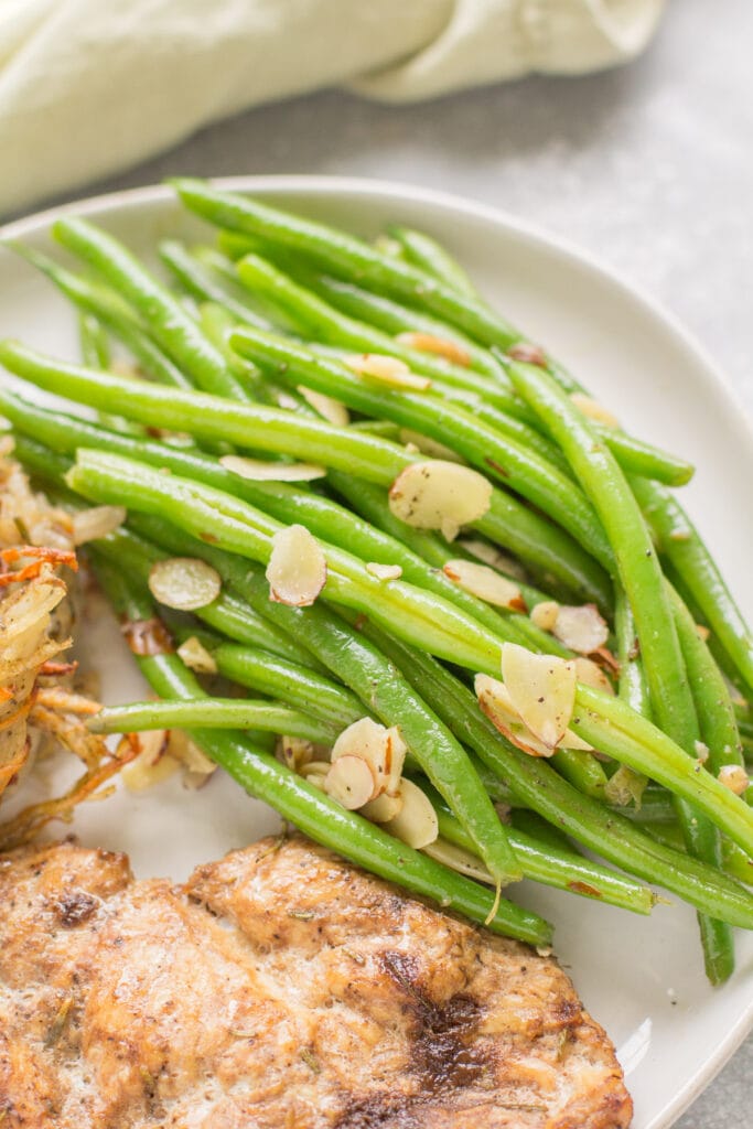 Green beans almondine on a plate next to potatoes and chicken