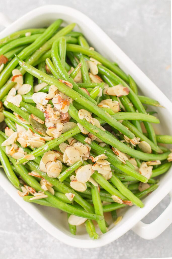 An overhead shot of delicious healthy green beans almondine in a white dish on a grey backgground