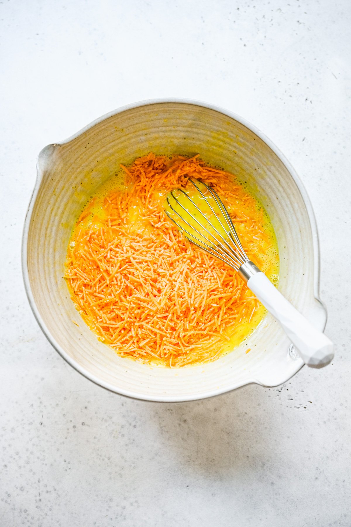 shredded cheddar cheese being mixed into egg mixture for keto frittata