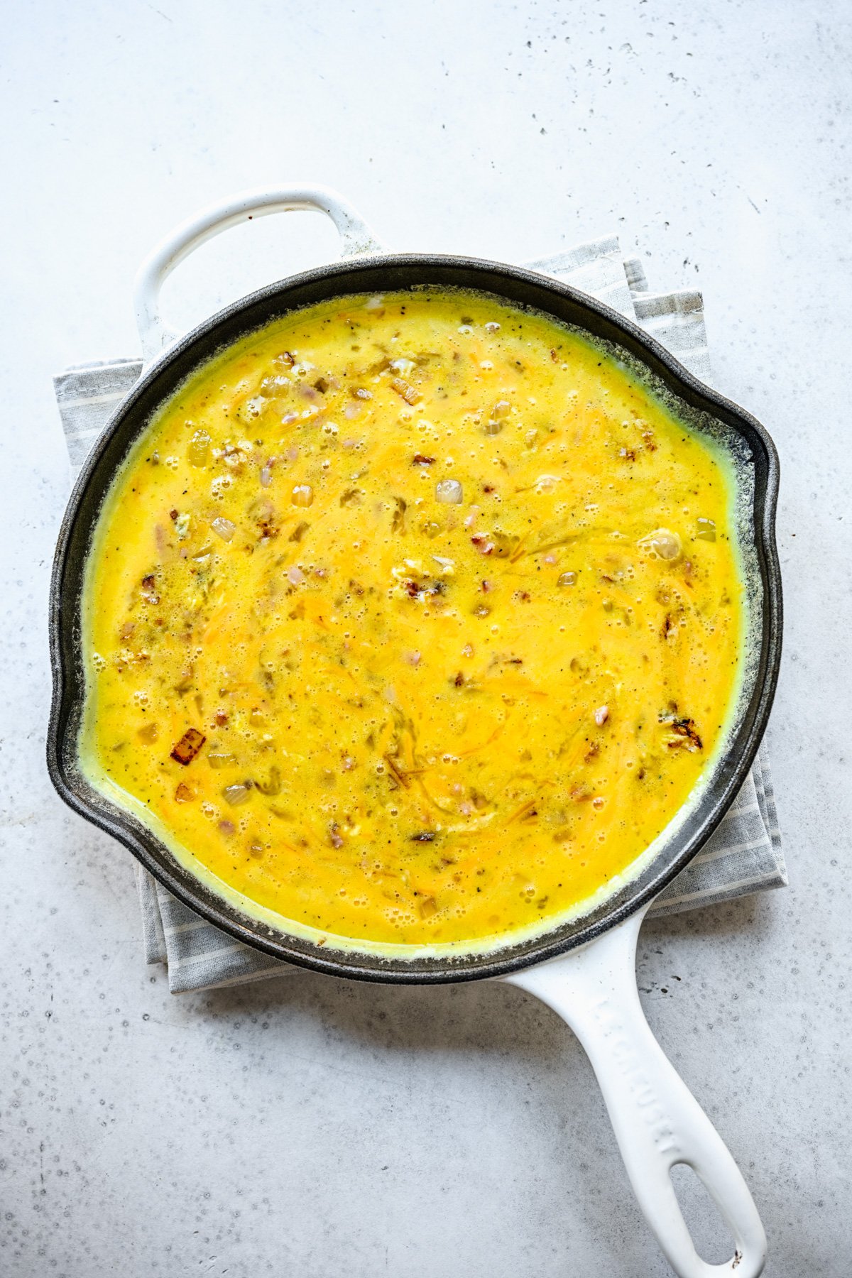 raw egg mixture added to onions and ham in a cast iron skillet to make a ham and cheese frittata