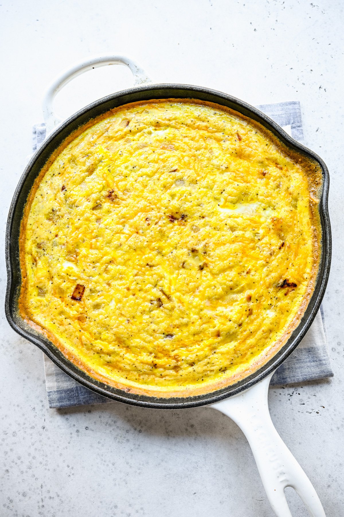An overhead shot of a cast iron pan of ham and cheese frittata on a white background