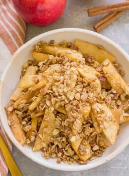 Healthy Apple Crisp in a white bowl on a grey background with apples off to the side