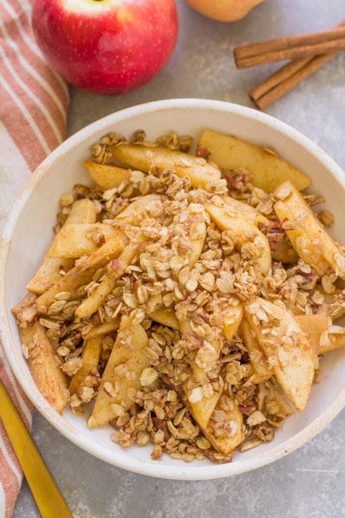 Healthy Apple Crisp in a white bowl on a grey background with apples off to the side