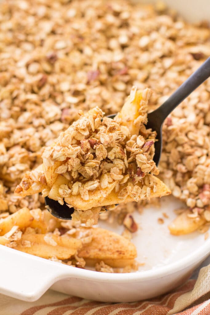 A black serving spoon taking a scoop out of Healthy Apple Crisp