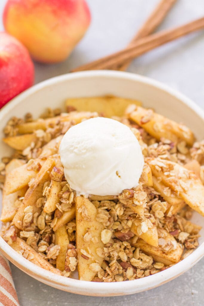 Healthy Apple Crisp in a bowl with a scoop of vanilla ice cream melting on top of it.