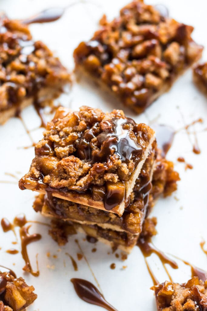 A close up image of paleo apple crumble bars stacked up and drizzled with caramel sauce.
