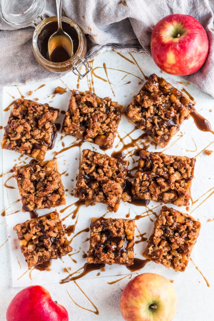 An overhead shot of 9 Healthy Apple Pie Bars on a white background. Caramel is drizzled everywhere