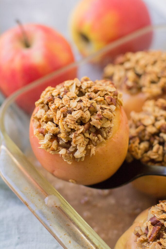 A black serving spoon taking a healthy baked apple out of a glass baking dish.