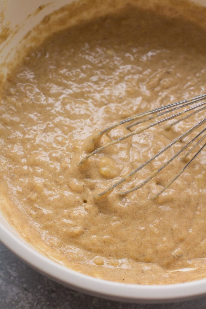A close up of healthy banana muffin batter in a white bowl with a whisk in it.