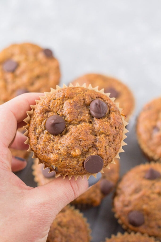 A hand holding up a Healthy Banana Muffin with more muffins in the background