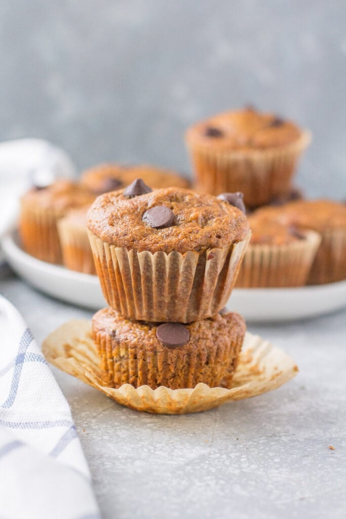 A front image of two banana muffins stacked on top of one another with a plate in the background