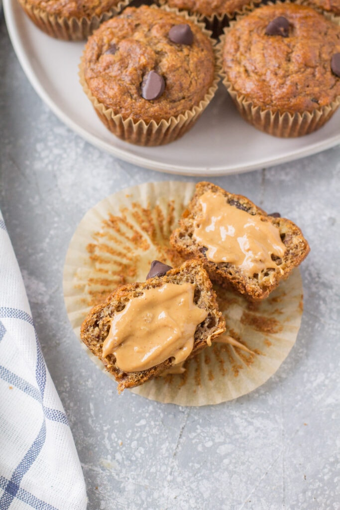 A banana muffin cut in half on a muffin liner with peanut butter on it - a healthy snack!