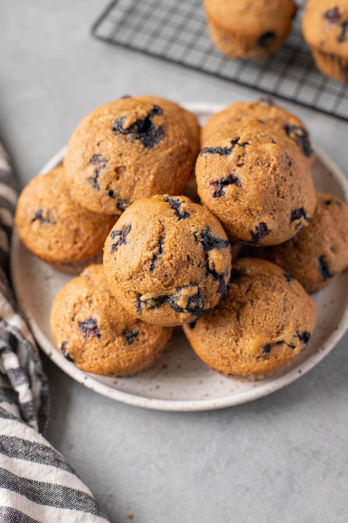 A close up of Healthy Blueberry Muffin Recipe on a white plate on a grey background with a striped linen off to the side