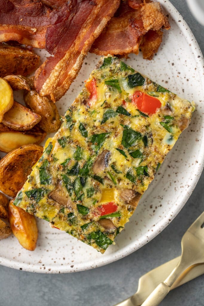 a piece of healthy breakfast casserole on a white plate with bacon and crispy potatoes on the side