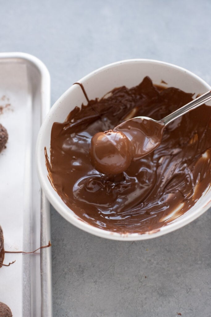 A brownie truffle being dipped into a bowl of melted chocolate