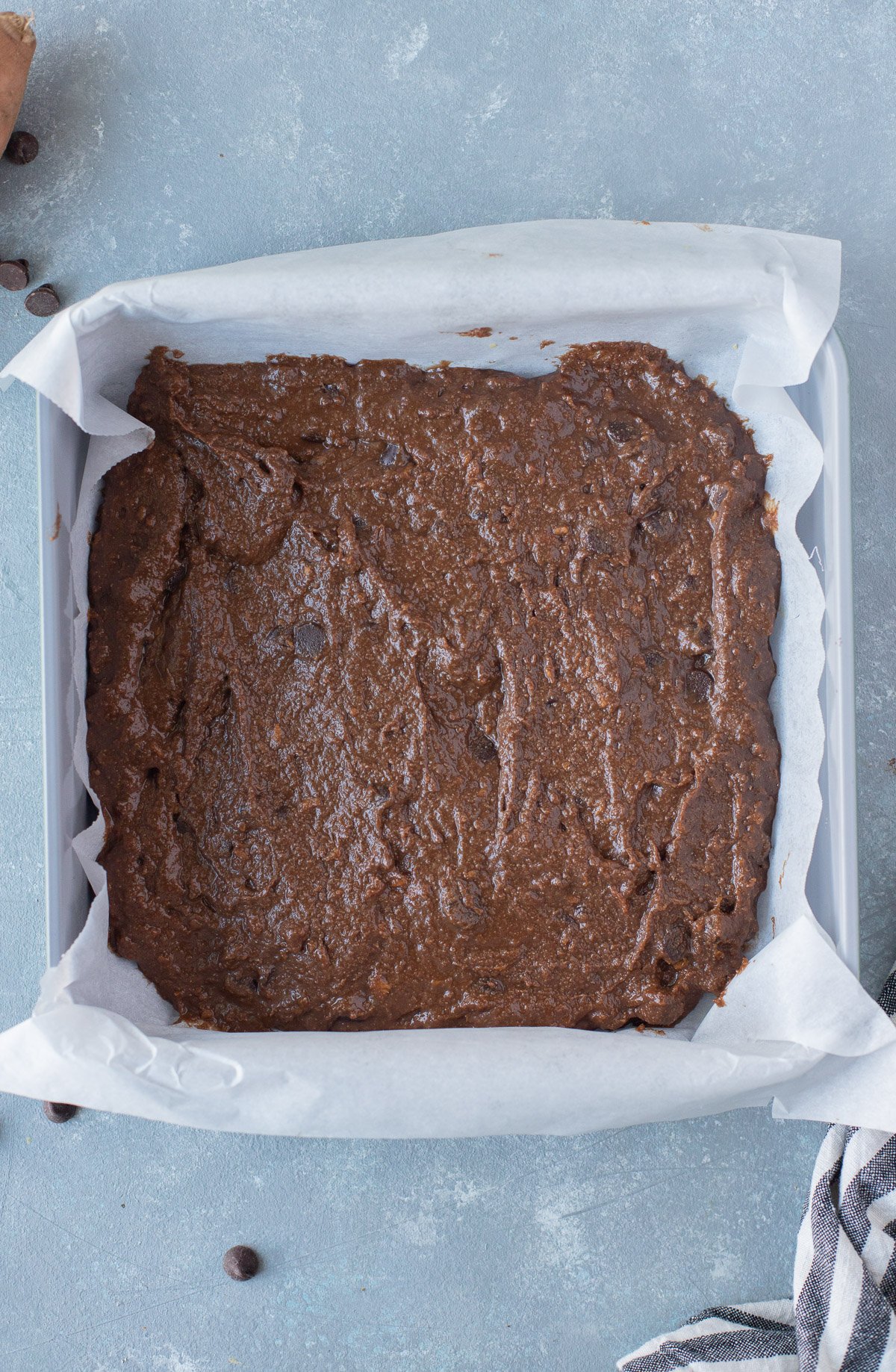 Sweet potato brownies batter in a parchment lined pan on a grey background