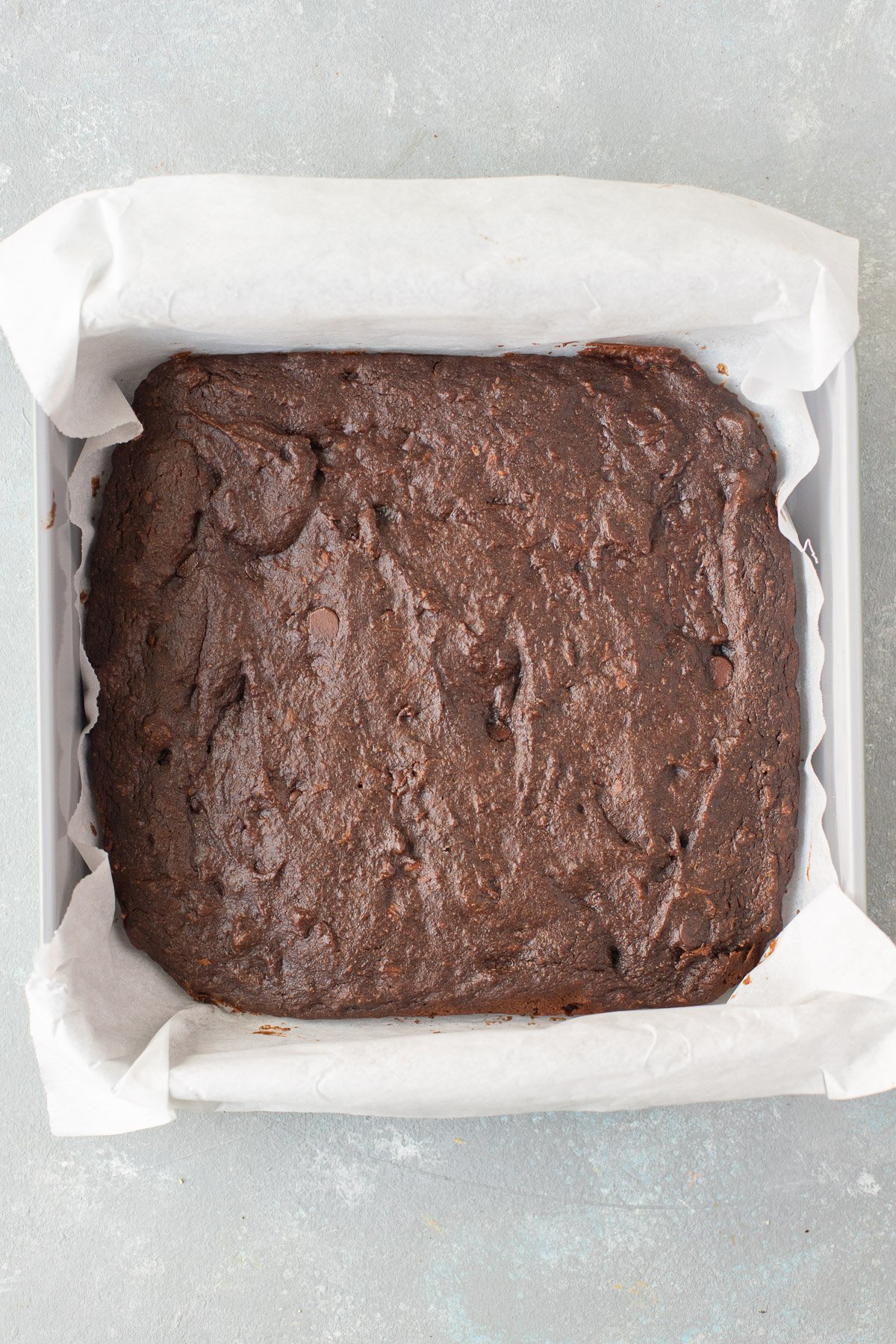 Sweet potato brownies in a parchment lined pan before cutting on a grey background