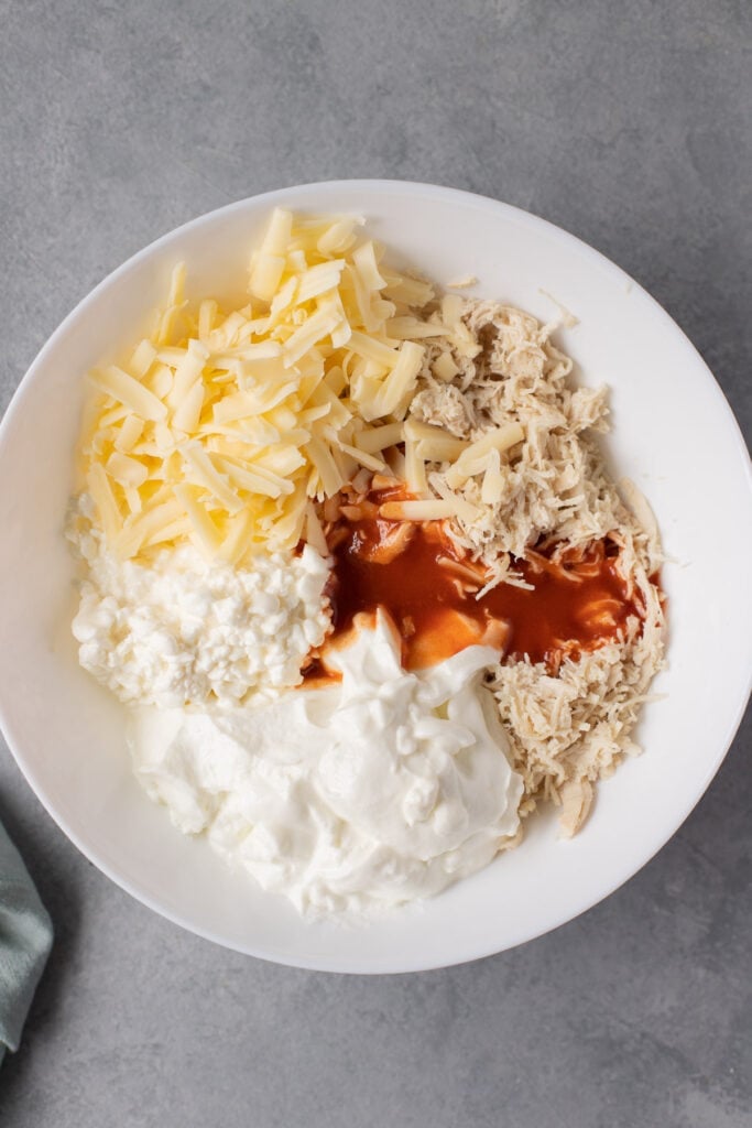 A collage showing step by step instructions on how to make healthy buffalo chicken dip. overhead shot showing ingredients segmented in white bowls